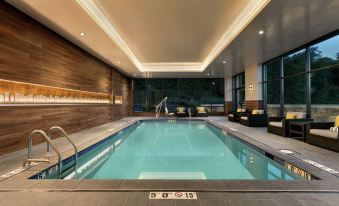 an indoor swimming pool surrounded by a lounge area , with several people relaxing and enjoying the space at Embassy Suites by Hilton Berkeley Heights
