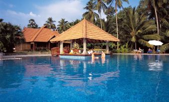 a large swimming pool surrounded by palm trees , with a gazebo and lounge chairs placed around it at Poovar Island Resort