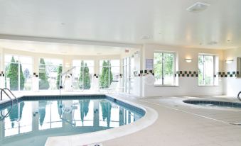 an indoor swimming pool with a hot tub , surrounded by white walls and large windows at Hilton Garden Inn Wooster