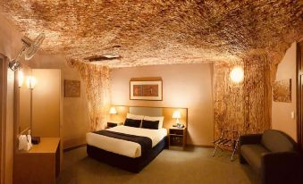 a hotel room with a bed , nightstands , and a couch , all under a thatched ceiling at Desert Cave Hotel