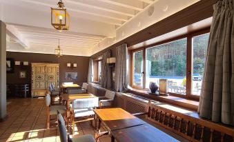 a cozy restaurant with wooden tables and chairs , large windows , and a view of trees at Parador de Gredos