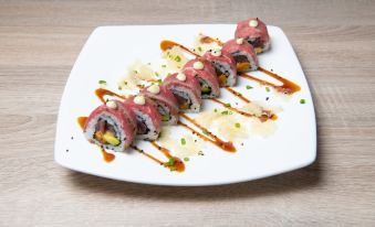 a white plate with several pieces of sushi on it , topped with sauce and garnished with sesame seeds at Kunuku Resort All Inclusive Curacao, Trademark by Wyndham