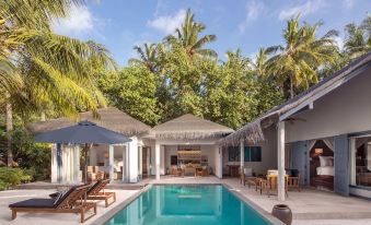 a large swimming pool is surrounded by lounge chairs and umbrellas , with a house in the background at Raffles Maldives Meradhoo Resort