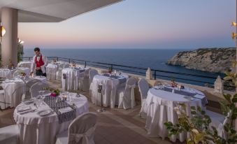 a dining area with tables and chairs set up on a rooftop , overlooking the ocean at Athina Palace Resort & Spa