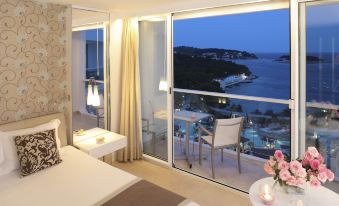 a luxurious hotel room with a large bed , a dining table , and a balcony overlooking the ocean at Amfora Hvar Grand Beach Resort