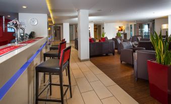 a modern hotel lobby with red and black furniture , including a couch , chairs , and a dining table at Holiday Inn Express Warwick - Stratford-Upon-Avon