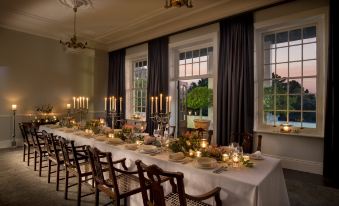 a long dining table set for a formal dinner , with multiple chairs surrounding it and lit candles adding a warm and inviting atmosphere at The Cellars-Hohenort