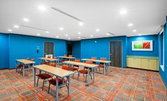 a conference room with blue walls , orange chairs , and tables , along with a television mounted on the wall at Home2 Suites by Hilton Gonzales