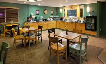a dining area with wooden tables and chairs , as well as a kitchen with a counter and various appliances at AmericInn by Wyndham Anamosa