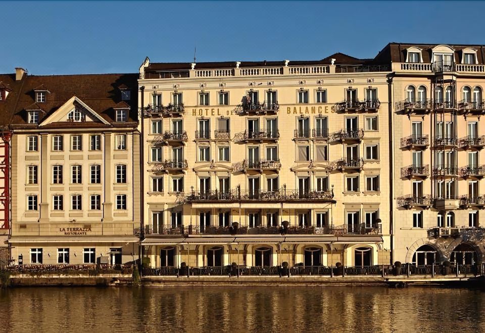 "a large building with balconies and a river in front , reflecting the hotel name "" hotel basen "" on a clear blue sky" at Hotel des Balances