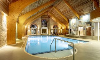 a large indoor swimming pool with a curved edge , surrounded by wooden beams and a stone wall at Cbh Park Farm Hotel