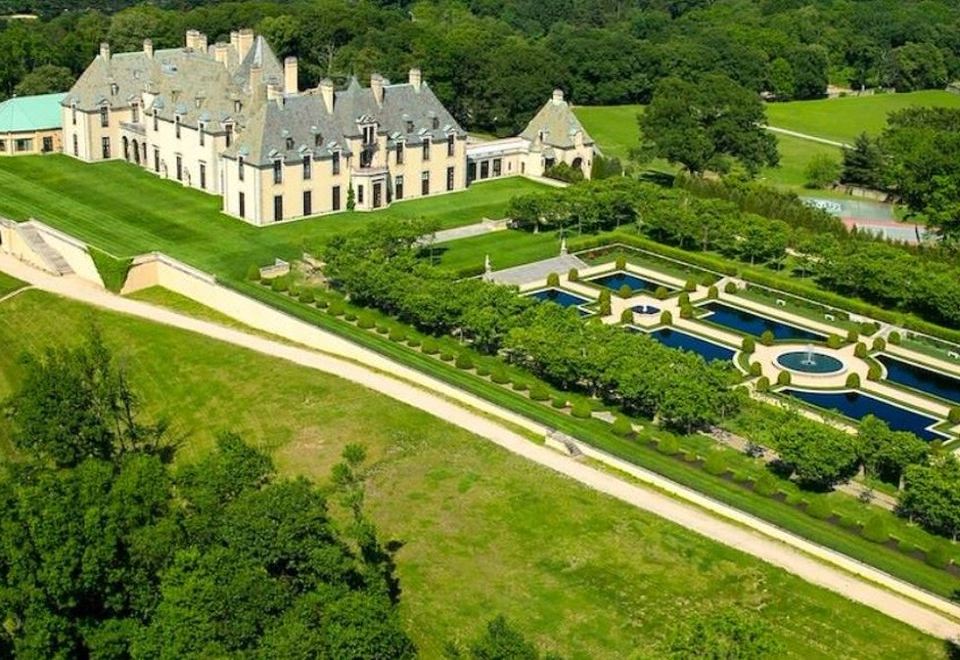 aerial view of a large mansion surrounded by green grass and trees , with a pond in the foreground at Oheka Castle Hotel & Estate