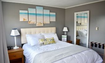 a cozy bedroom with a large bed , white linens , and a painting of the beach on the wall at Friars Bay Inn & Cottages