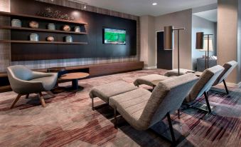 a modern living room with a large flat - screen tv mounted on the wall , along with several chairs and couches at Courtyard Schenectady at Mohawk Harbor
