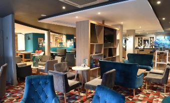 a modern lounge area with blue and gray seating , wooden shelves , and a bar in the background at Holiday Inn Glasgow - East Kilbride