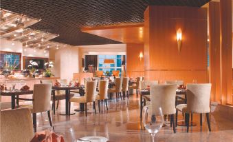 a large , well - lit restaurant with multiple dining tables and chairs , as well as wine glasses and utensils at Oakwood Premier Cozmo Jakarta