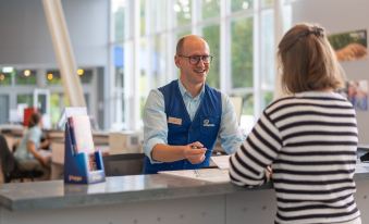 a man in a blue vest is standing at a hotel reception desk , checking in a woman at Sunparks Kempense Meren