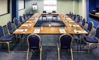 "a large conference room with a long wooden table , blue chairs , and a projector screen displaying "" mercure "" on the wall" at Mercure Swansea Hotel