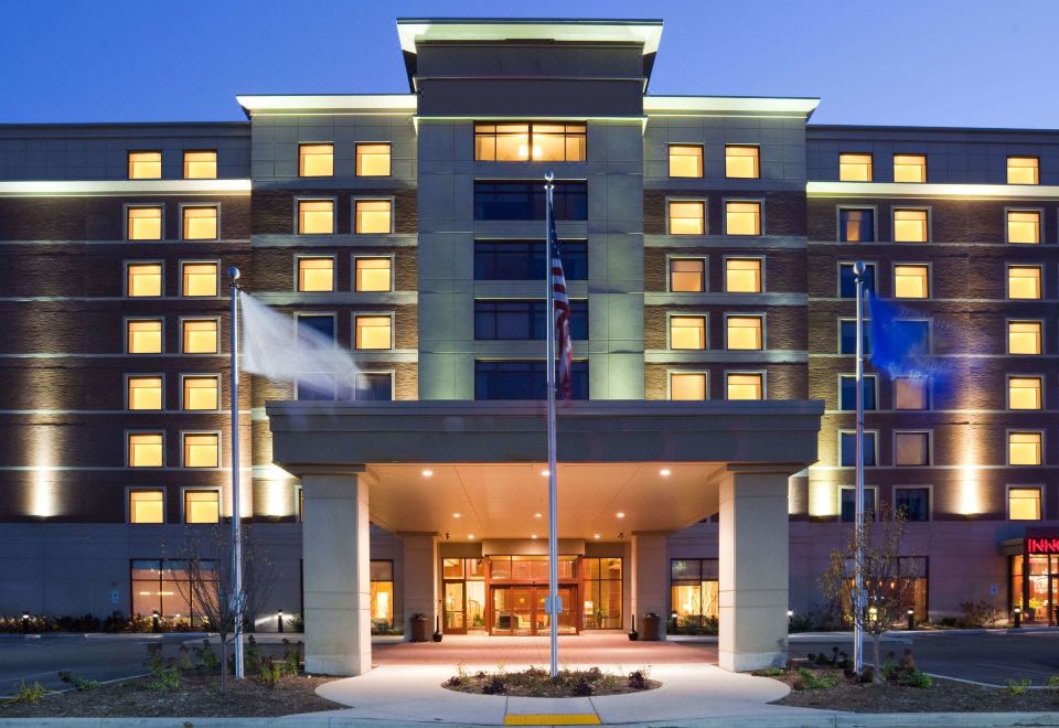 a modern hotel building with its lights illuminating the exterior , and the front entrance decorated with flags at Sonesta Milwaukee West Wauwatosa