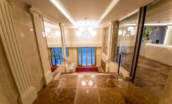 a grand foyer with a red carpeted floor , white walls , and a large window overlooking the ocean at NH Geneva City