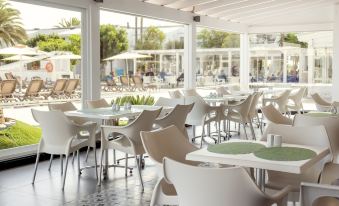 a modern restaurant with white tables and chairs , large windows , and a view of the outdoors at Playa Park Zensation