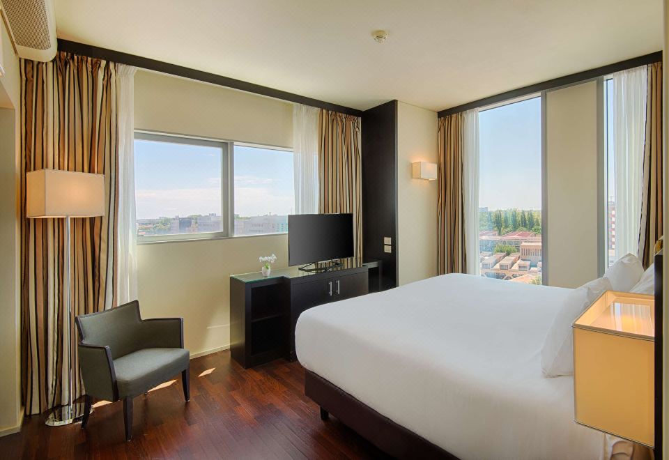 a modern hotel room with a large window , wooden floor , and white bed , along with a tv , desk , and chair at NH Padova