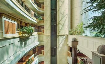 a tall , multi - level building with many balconies and greenery , as well as potted plants in the atrium at Hilton Beirut Metropolitan Palace