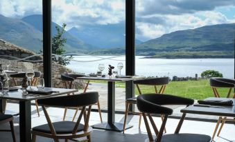 a table with chairs is set up in front of a window overlooking a lake and mountains at Isle of Raasay Distillery