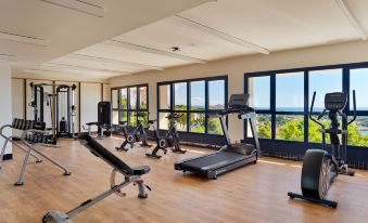 a well - equipped gym with various exercise equipment , including treadmills and weightlifting machines , positioned near large windows that offer views of the outdoors at H10 Imperial Tarraco