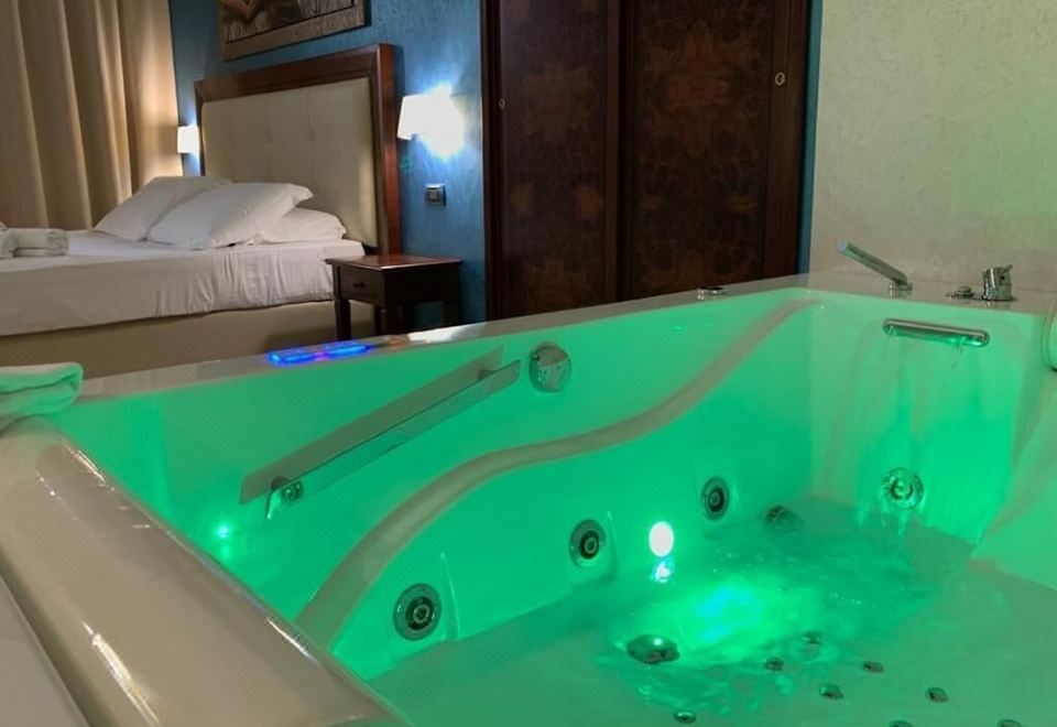 a large , dimly lit bathtub with a green light and two hands on the side at Hotel Flora
