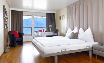 a bedroom with a large bed and white linens , a window overlooking the ocean , and a couch at Alpenblick Weggis - Panorama & Alpen Chic Hotel