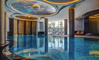 a modern indoor swimming pool with blue water and gold accents , surrounded by large windows and comfortable seating at Sheraton Grand Adana