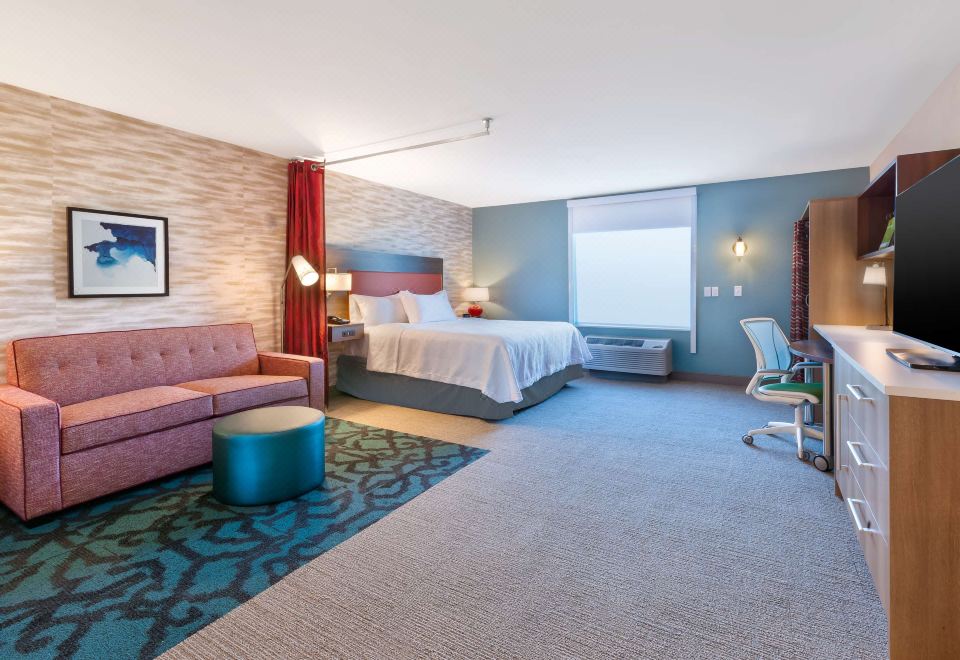 a modern hotel room with a large bed , couch , and living area , decorated with blue walls and carpet at Home2 Suites by Hilton Battle Creek