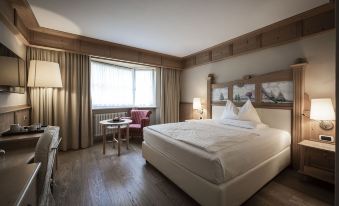 a large bed with white linens is in a room with wooden floors and furniture at Adler Spa Resort Dolomiti
