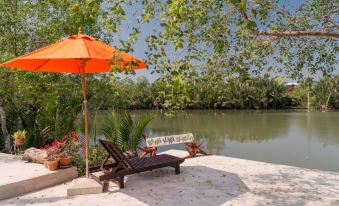 "a beach scene with a wooden deck , an orange umbrella , and a sign that says "" stay here "" on the sand" at Baan Suan Nuanta