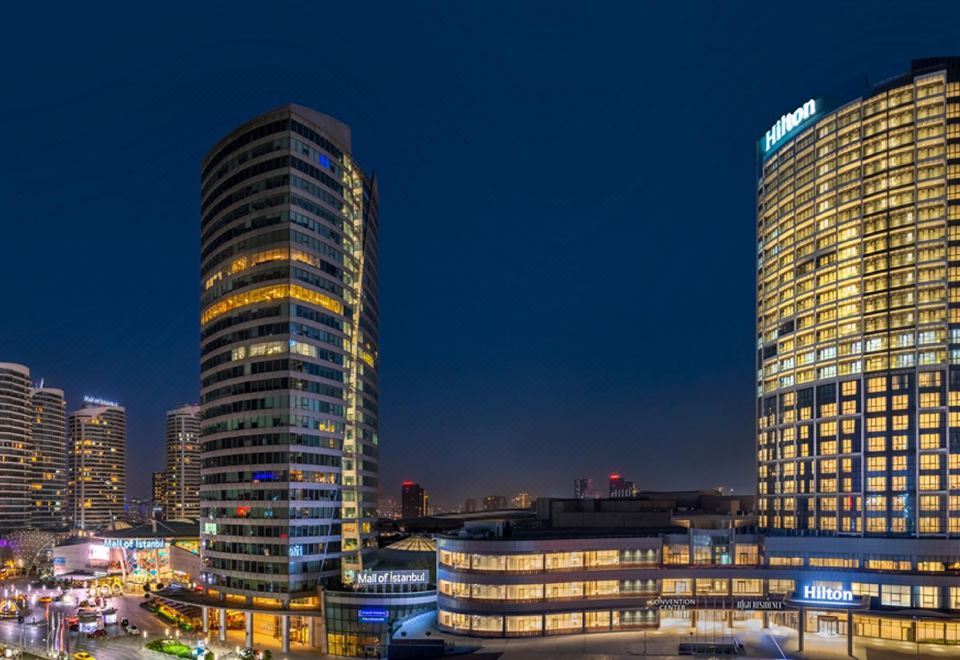 a city skyline at night , with two tall buildings illuminated by bright lights against the dark background at Hilton Mall of Istanbul