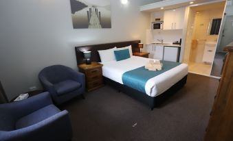 a modern hotel room with a large bed , blue and white bedding , and a blue chair at Kallangur Motel