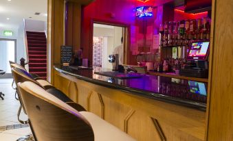 a bar with a long wooden counter and chairs , along with various bottles and glasses on the counter at Kilmorey Arms Hotel