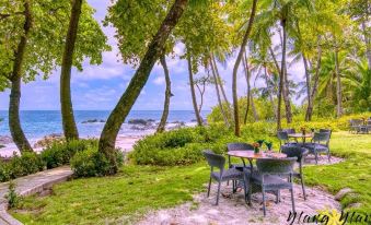 a serene beach scene with a table and chairs set up on the grass , overlooking the ocean at Ylang Ylang Beach Resort