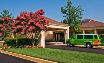 a green van is parked in front of a building with trees and flowers surrounding it at Courtyard New Carrollton Landover