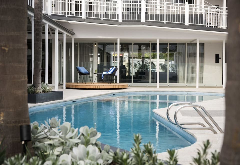 an outdoor swimming pool surrounded by a patio area , with several lounge chairs placed around the pool at Tradewinds Hotel and Suites Fremantle
