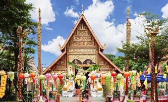 a traditional thai temple with wooden buildings , green trees , and colorful decorations , set against a blue sky at Diamond Park Inn Chiangrai & Resort