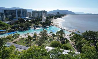 a beach with palm trees , a large pool , and a city in the background , as well as mountains in the distance at Pacific Hotel Cairns