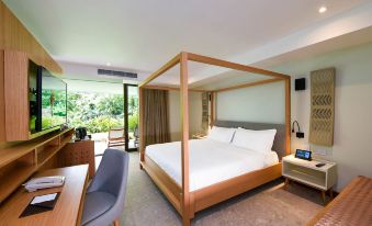 a large bed with a wooden frame and white sheets is in a room with a chair , desk , and sliding glass door at Tabacon Thermal Resort & Spa