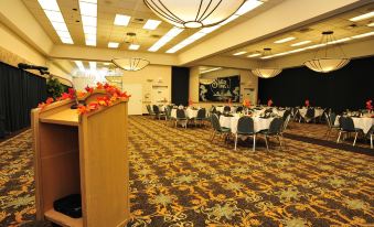 a large dining room with multiple tables and chairs , a podium in the center , and pendant lights hanging from the ceiling at Shilo Inn Suites Klamath Falls