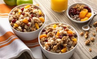 a wooden table topped with two bowls of oatmeal , each containing different types of granola and fruit at Home2 Suites by Hilton Dekalb