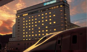 "a train passing by a large building with the name "" clipper "" on it , with a beautiful sunset in the background" at Hotel Metropolitan Nagano