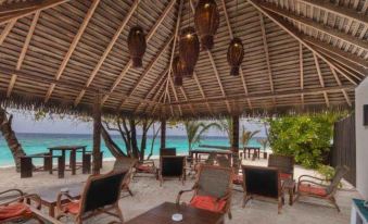 a thatched - roof hut on a sandy beach , with several chairs and tables set up for guests at Filitheyo Island Resort