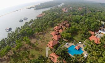 a bird 's eye view of a resort with red roofed buildings , palm trees , and a swimming pool surrounded by water at Poovar Island Resort