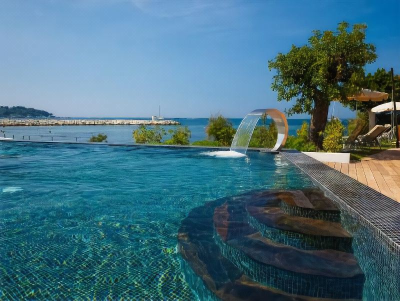 a large outdoor swimming pool surrounded by trees , with a water slide visible in the background at Cap d'Antibes Beach Hotel